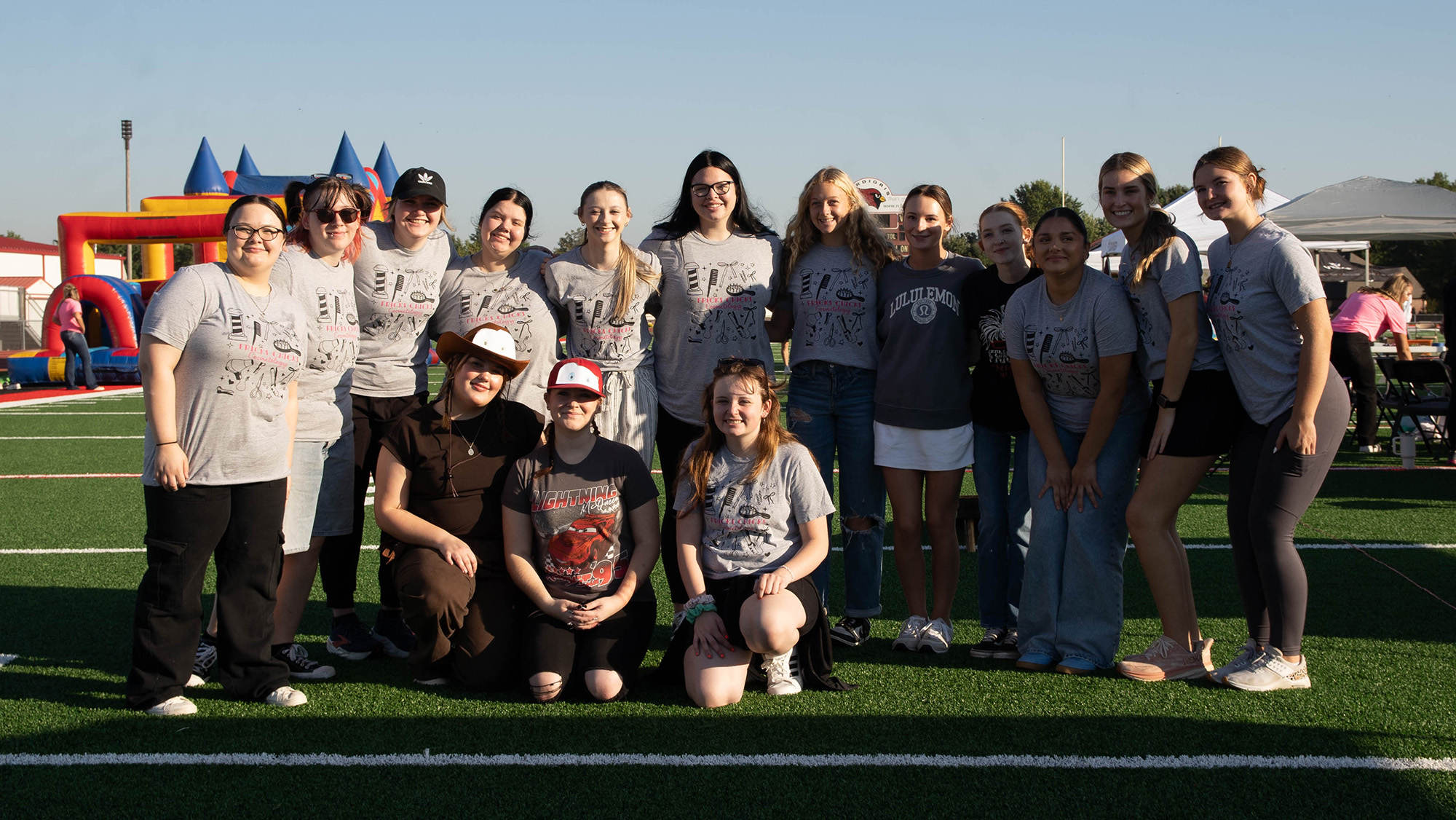 Central Tech Drumright cosmetology students volunteer at the Gold4Kids Foundation of Tulsa Gold4Kids Walk at Verdigris High School, smiling together on the field with inflatable bounce houses in the background.