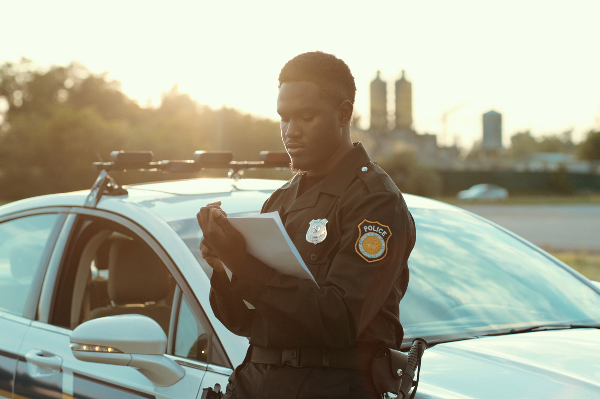 man leaning against car writing a report