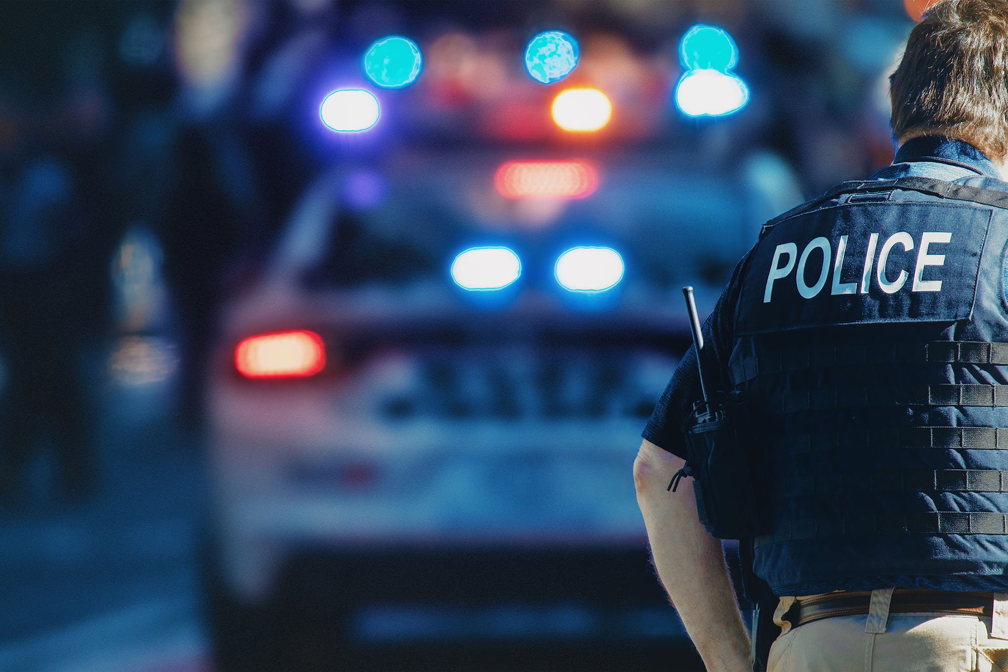 picture of a police officer near a cop car with lights on